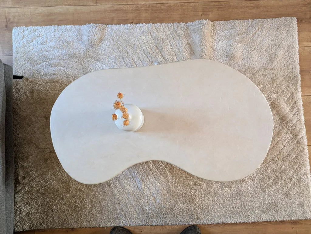 Vue aérienne de la table basse Florence avec son plateau organique en argile et quartz, posée sur un tapis doux pour une ambiance cosy et naturelle.