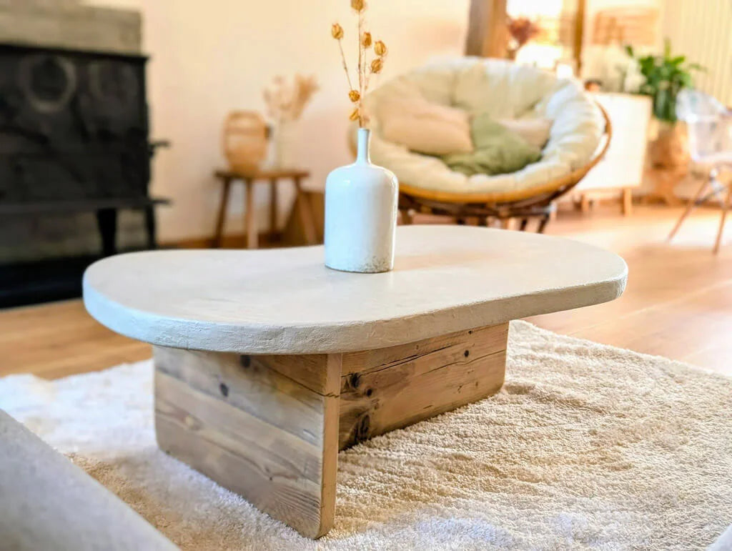 Table basse Florence en bois recyclé avec plateau en argile et quartz, mise en scène dans un salon chaleureux avec un fauteuil bohème et un poêle en fonte.